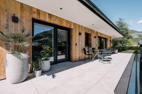 Sonnige Terrasse mit Hebeschiebtür und Fassade aus Holz